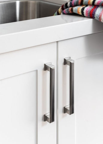Close-up of white kitchen cabinets with metallic handles and a colorful towel on a shelf.