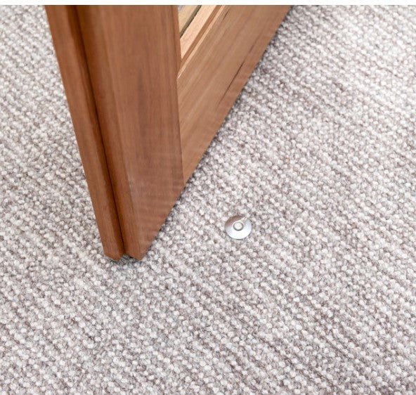 Close-up of a carpeted floor with a wooden baseboard and a small metal object.