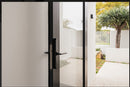 Modern glass door with black frame leading to a garden with trees and a white fence.